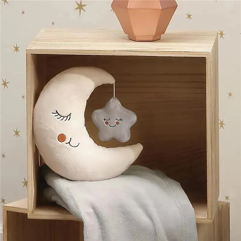 Plush moon pillow with a smiling face and a hanging star ornament in a wooden shelf, accompanied by a soft blanket.