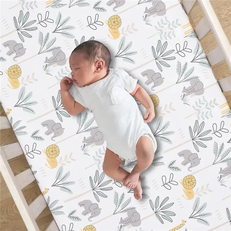 Lambs & Ivy Jungle Adventure crib sheet featuring playful elephants, lions, and foliage with a baby peacefully sleeping beside it.