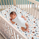 Fitted crib sheet featuring a colorful Lion King Adventure design with various characters and animals, with an infant sleeping on it.
