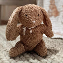 Organic cotton bunny plush in honey color, featuring floppy ears and a bow, sitting on a textured blanket.