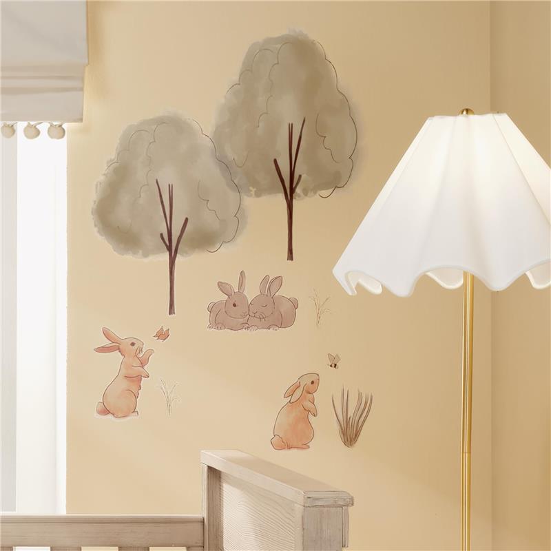 Wall decals featuring playful bunnies, trees, and grass, ideal for nursery decor by Lambs & Ivy.
