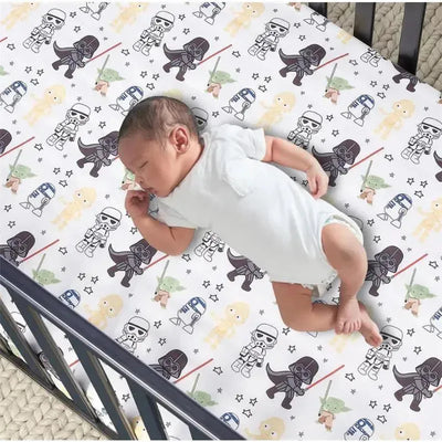Classic Star Wars crib sheet featuring characters like Darth Vader, Yoda, and Stormtroopers, with a sleeping baby.