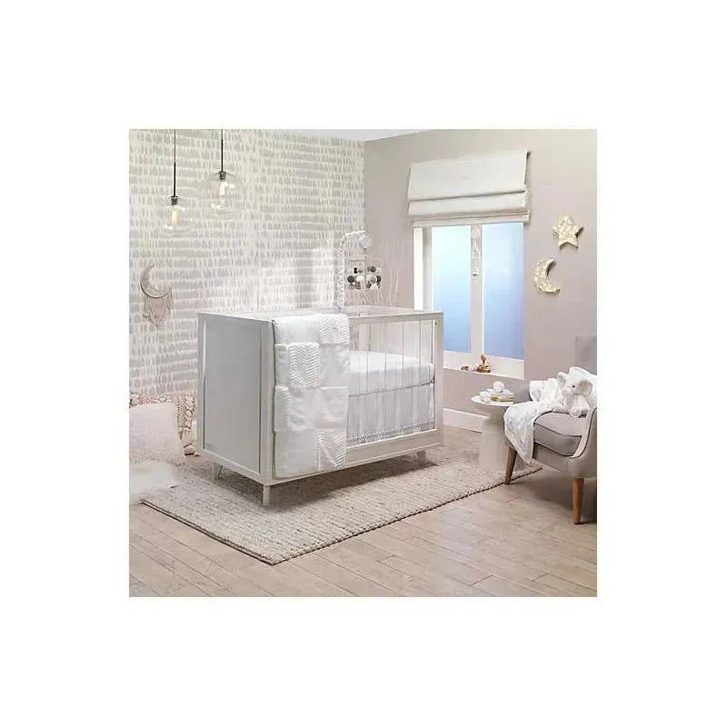 Lambs & Ivy white patchwork quilt draped over a modern crib in a stylish nursery setting with soft lighting and decor.