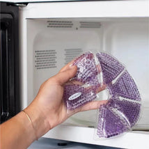 Hand holding a Lansinoh Therapearl 3-IN-1 Breast Therapy pack, showing purple gel beads, inside a microwave.