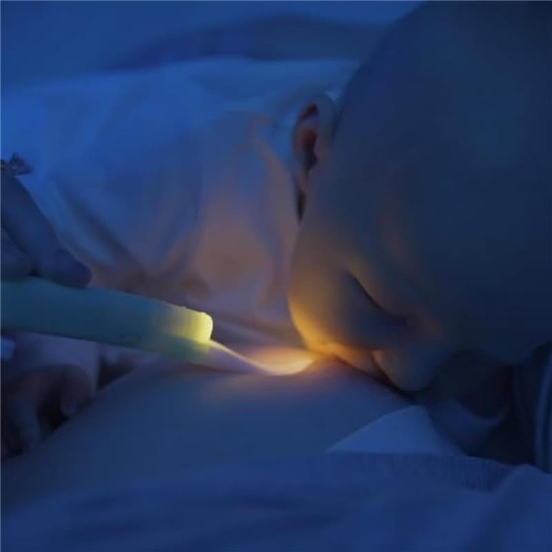 A baby breastfeeding in a dimly lit room, illuminated by a Latchlight wearable baby night light held by an adult.