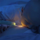 A baby breastfeeding in a dimly lit room, illuminated by a Latchlight wearable baby night light held by an adult.