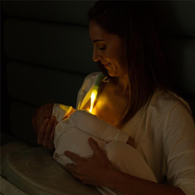 Mother breastfeeding a baby in low light, with the Latchlight wearable night light illuminating their interaction.