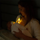 Mother breastfeeding a baby in low light, with the Latchlight wearable night light illuminating their interaction.