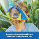 A child holds the Learning Resources Geosafari Bugservatory up to their face, examining leaves through the magnifying lens, set against green foliage.