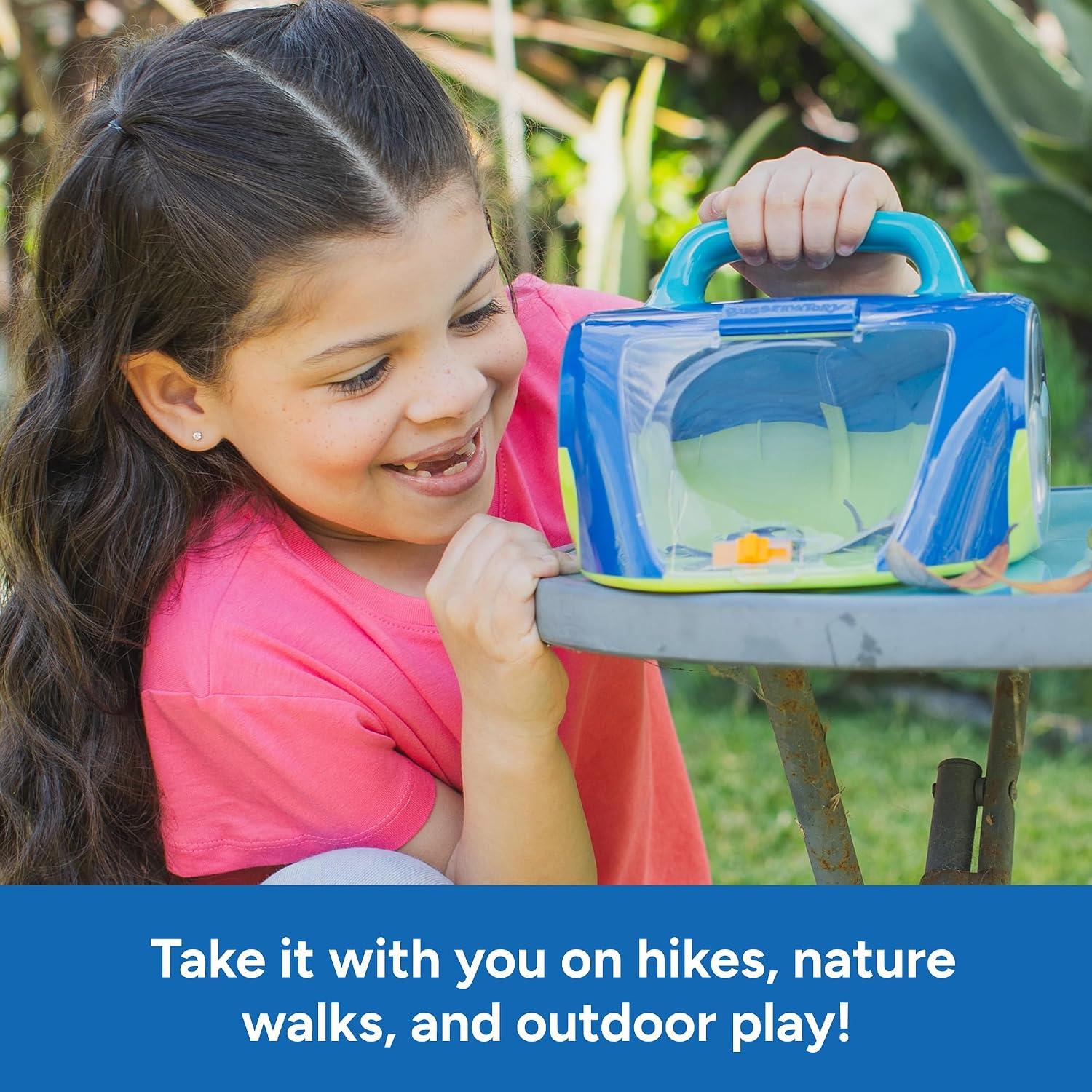Girl in a pink shirt smiles while holding a blue and green Geosafari Bugservatory on a table outdoors.
