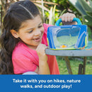 Girl in a pink shirt smiles while holding a blue and green Geosafari Bugservatory on a table outdoors.