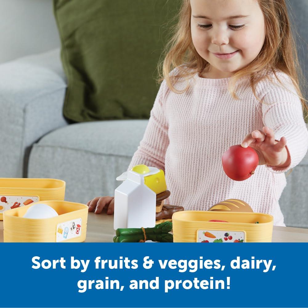 A child sorts colorful plastic food items into containers labeled for fruits, vegetables, dairy, grain, and protein.