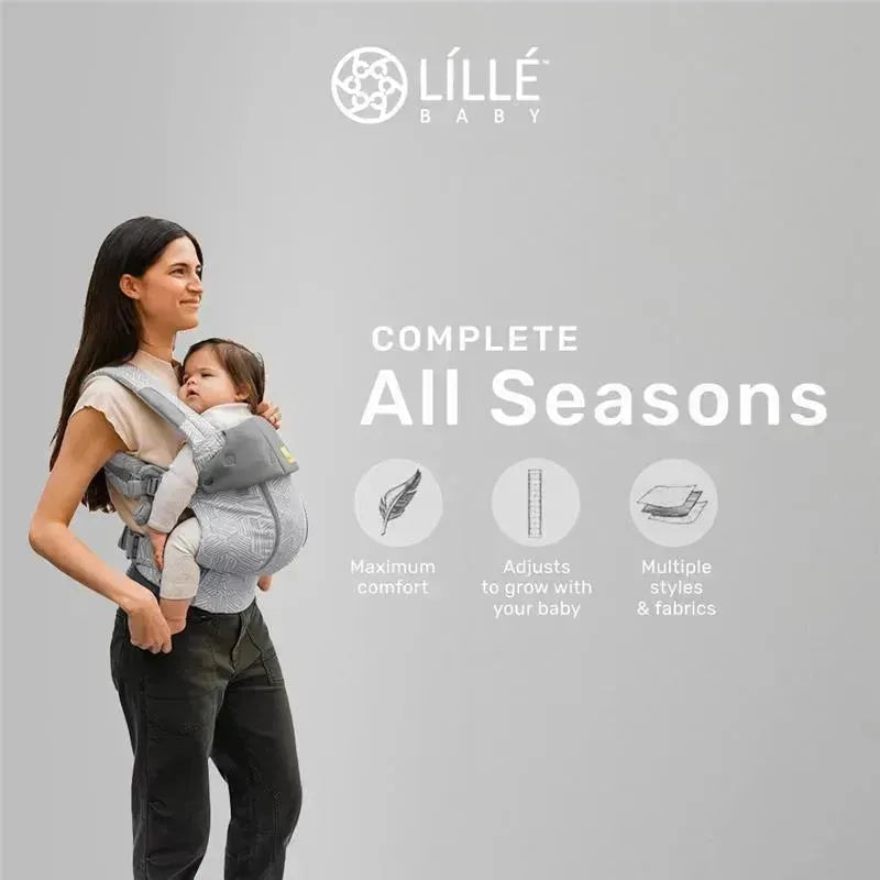 Mother wearing a Líllé Baby Complete All Seasons Carrier in Pebble Grey, holding a baby with text highlighting comfort and adjustability.