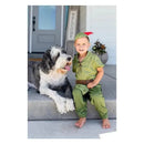 Child in a green Peter Pan costume sits next to a large dog, both smiling on a porch.