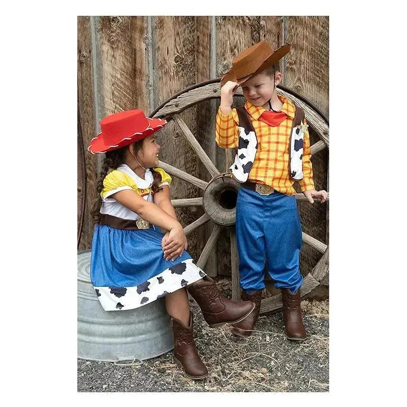 Kids dressed in cowboy costumes: a girl in a cow-patterned dress and red hat, and a boy in a plaid shirt and cowboy hat, smiling.