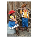 Kids dressed in cowboy costumes: a girl in a cow-patterned dress and red hat, and a boy in a plaid shirt and cowboy hat, smiling.