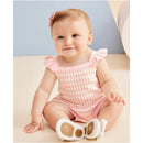 Baby girl in a pink striped bubble outfit with ruffled straps, sitting on a light-colored surface, smiling.