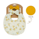 Floral cotton bib with pom-pom trim, paired with two mustard bows, showcasing front and back design details.