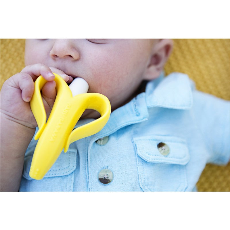 Infant holds a yellow banana-shaped brush in their mouth, designed for teething and dental hygiene.
