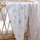 Two soft Jersey swaddles in a crib; one features sloths and rainbows, the other has a simple rainbow pattern.