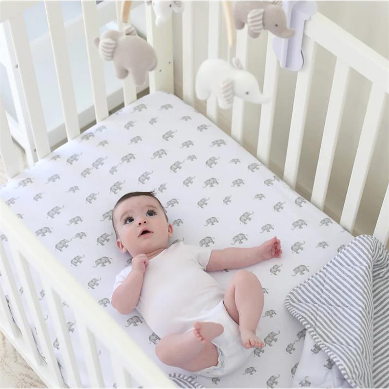 A baby lying in a crib with a musical mobile featuring elephants, looking up with curiosity.
