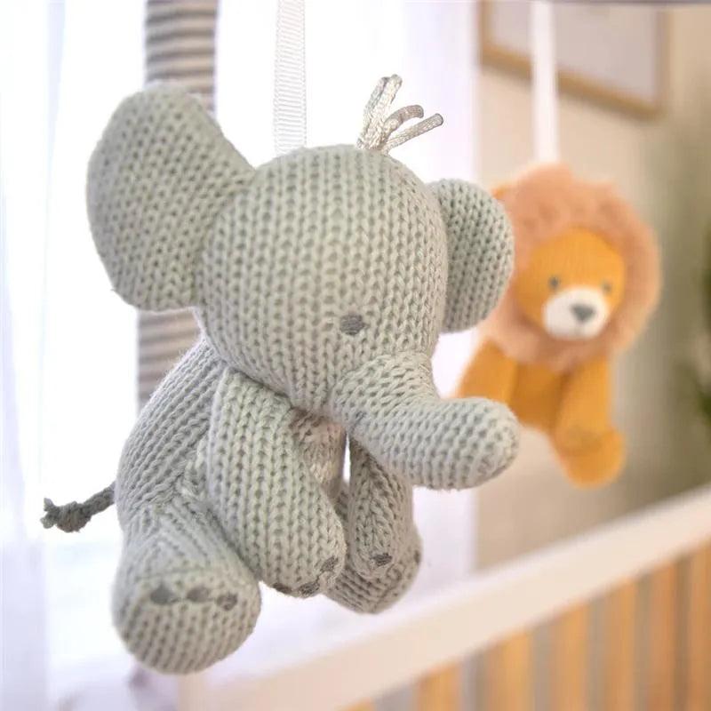 Soft knitted elephant and lion toys hanging from a musical mobile, designed for nursery decor.