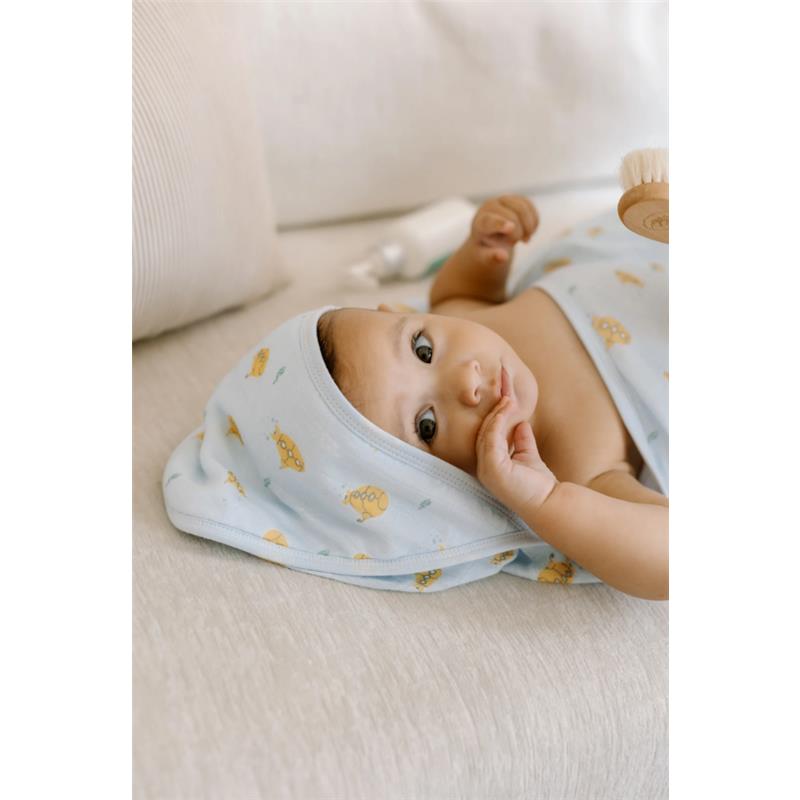 Hooded towel set in ocean explorer theme draped over a baby lying on a light-colored surface, sucking thumb.