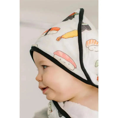 Hooded towel set featuring a baby happily wearing a towel adorned with colorful sushi prints.