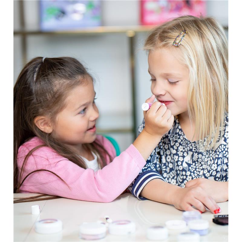 Two young girls applying makeup from the LunaStar Klee Eye Shadow and Lip Shimmer Holiday Gift Set on each other, with products visible on the table.