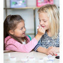 Two young girls applying makeup from the LunaStar Klee Eye Shadow and Lip Shimmer Holiday Gift Set on each other, with products visible on the table.