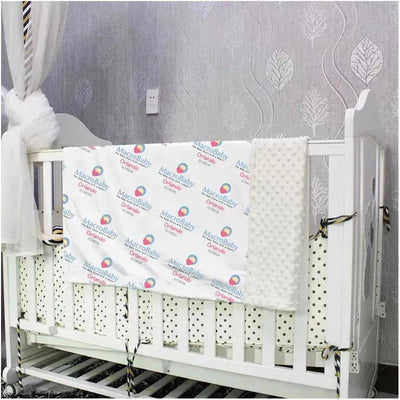 Soft baby blanket by Macrobaby, featuring a patterned design, draped over a white crib with a textured edge.