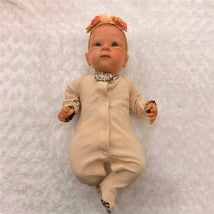 Reborn baby doll in a beige outfit with leopard print accents, featuring open green eyes and painted hair.