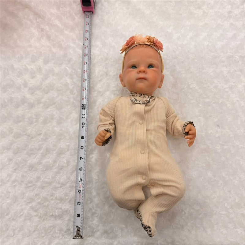 Reborn baby doll with painted hair, open green eyes, wearing a beige outfit with leopard print accents and a floral headband.
