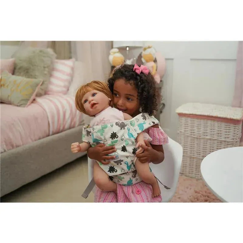 A young girl in a pink outfit carries a baby doll in a dinosaur-patterned maternity doll carrier, smiling happily.