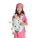 A girl in pink clothing holds a cuddly baby doll in a dinosaur-themed maternity carrier.
