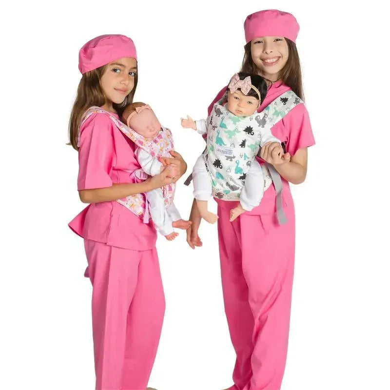 Two children in pink scrubs wear doll carriers; one carries a baby doll in a floral pattern, the other in a dinosaur print.