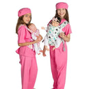 Two children in pink scrubs wear doll carriers; one carries a baby doll in a floral pattern, the other in a dinosaur print.