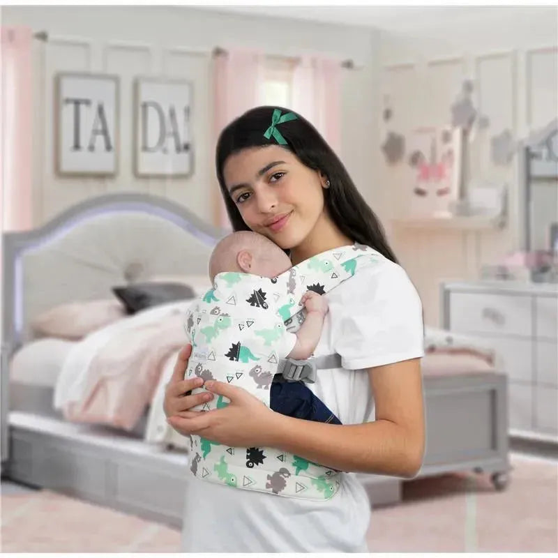 Maternity doll carrier featuring a girl holding a baby doll, both in a dinosaur-patterned wrap, in a pastel room setting.