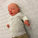 Reborn doll named Megan, made of white vinyl, with painted hair, opened blue eyes, wearing a white onesie.