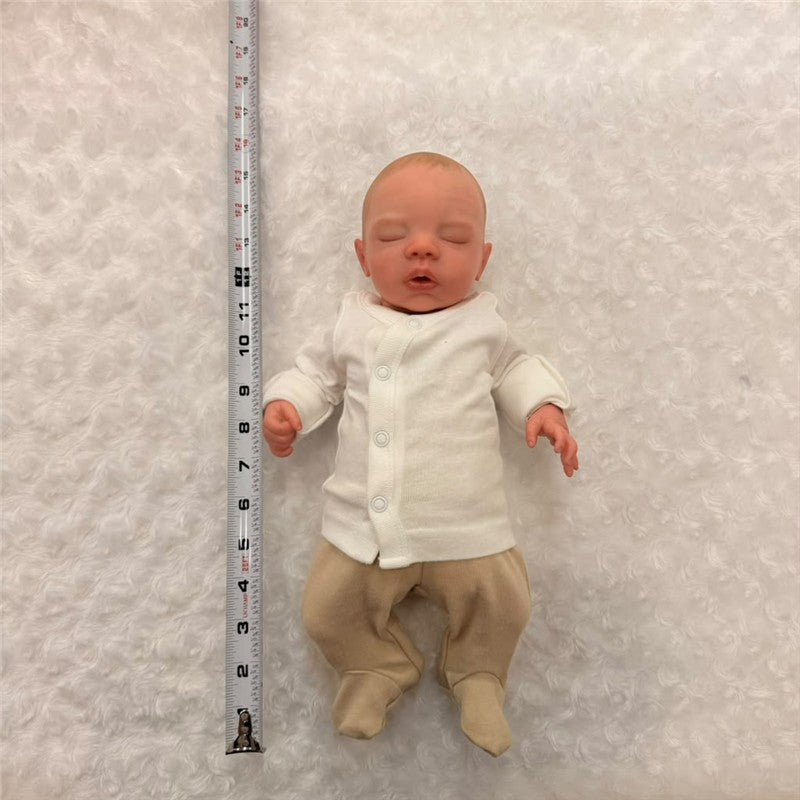 Macrobaby Reborn Doll named Megan, featuring white vinyl, painted hair, opened blue eyes, and dressed in a white onesie with beige pants.
