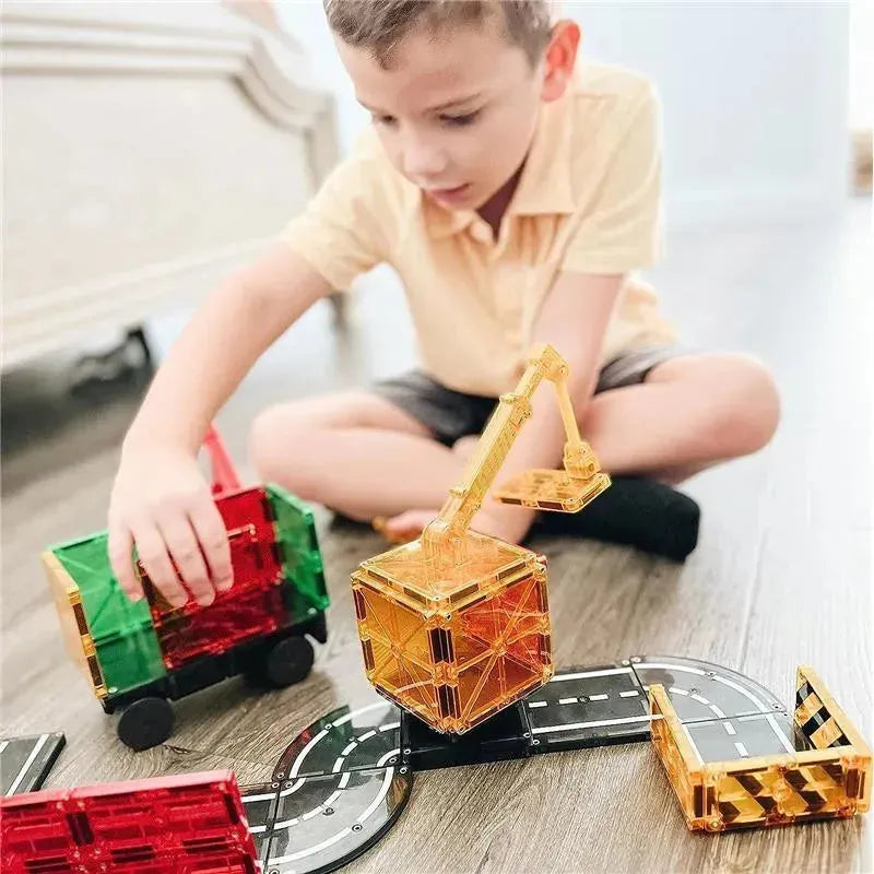 A child plays with a 32-piece Magnatiles set, building structures with magnetic blocks and toys, including a yellow crane and trucks.