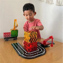 A child in a pink shirt builds a tall structure with colorful Magnatiles on a wooden table, featuring a toy truck and a crane.