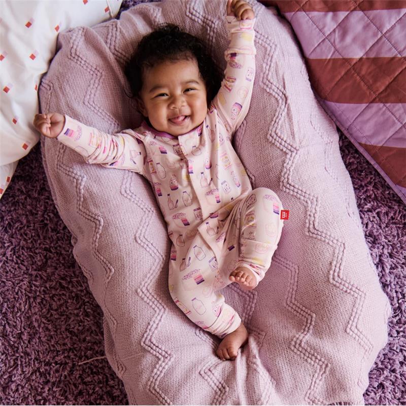 Smiling baby in a pink, patterned convertible coverall, lying on a cozy pink blanket, celebrating with raised arms.