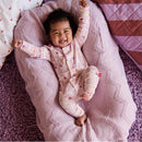 Smiling baby in a pink, patterned convertible coverall, lying on a cozy pink blanket, celebrating with raised arms.