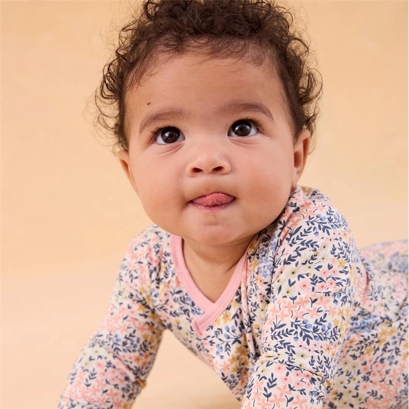 Baby wearing a floral-patterned Magnetic Me Chelsea Modal Convertible Coverall, smiling with tongue out.