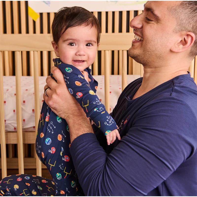 Father holds a smiling baby in a colorful modal convertible coverall, surrounded by a nursery-style background.