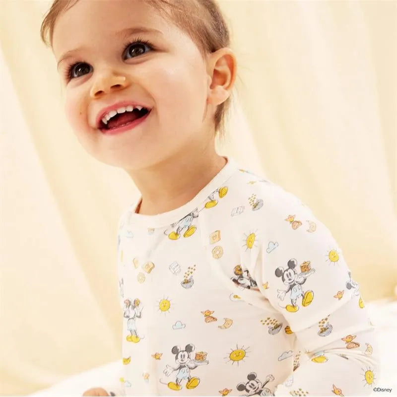 Toddler smiling while wearing a white modal coverall featuring Mickey Mouse and brunch-themed prints.