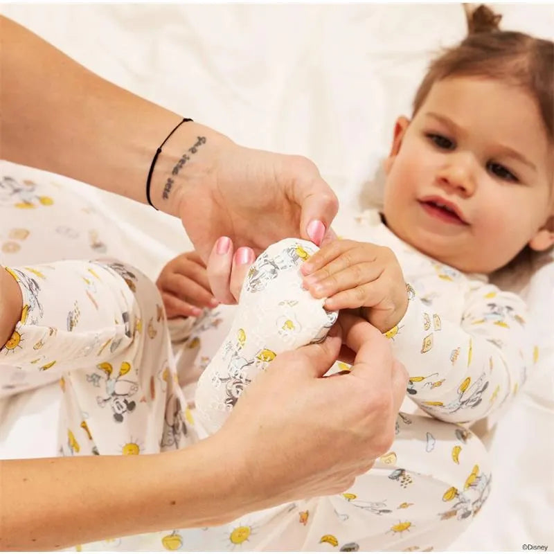 Toddler in Mickey-themed modal coverall having their foot examined by an adult, both smiling.