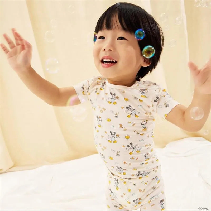 Child joyfully playing in a pajama set featuring Mickey Mouse illustrations, surrounded by colorful bubbles.