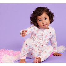 Toddler wearing Magnetic Me modal long sleeve pajamas with a pink ballerina print, sitting on a purple background and playful pose.
